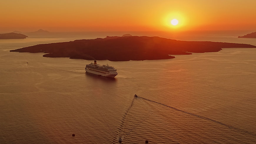 Cruise ship sailing past island at golden sunset