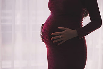 Pregnant woman holding belly in red dress by window