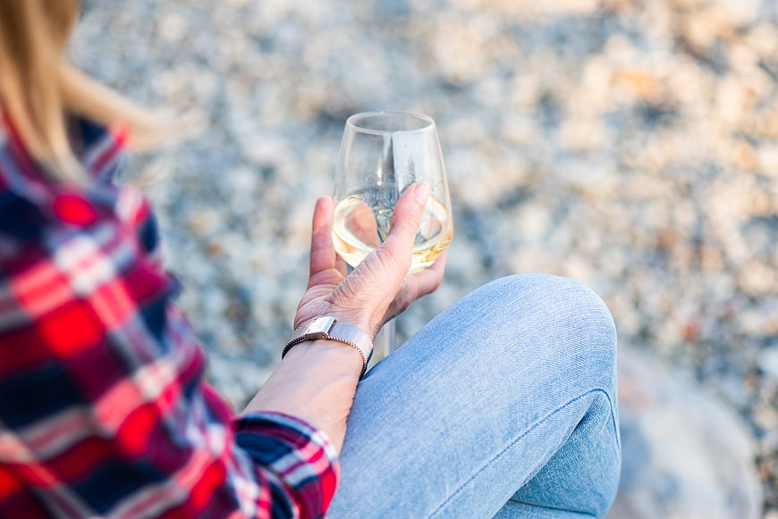 Woman holding white wine glass on pebble beach