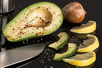 Sliced avocado with lemon wedges and knife on dark surface