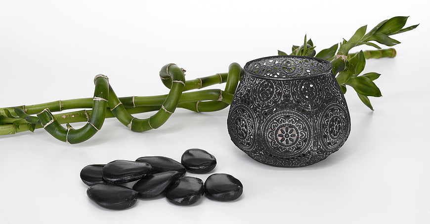 Lucky bamboo, black zen stones, and metal candle holder on white