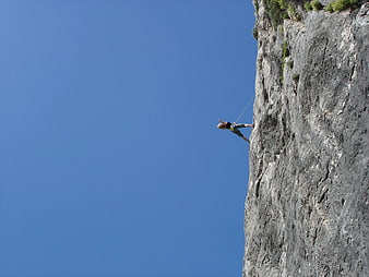 Rock Climber Scaling Cliff Face Against Blue Sky