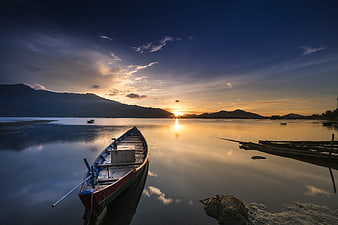 Traditional wooden boat on calm lake at sunset with mountains