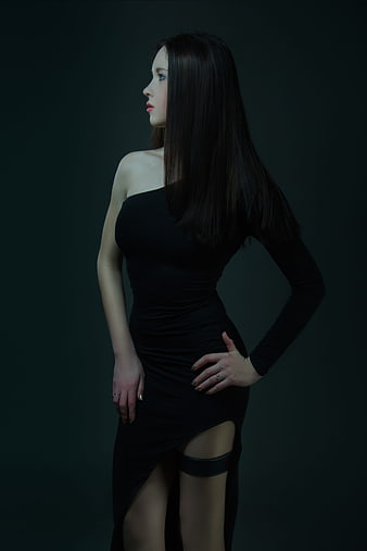 Elegant young woman in black one-shoulder dress against dark background