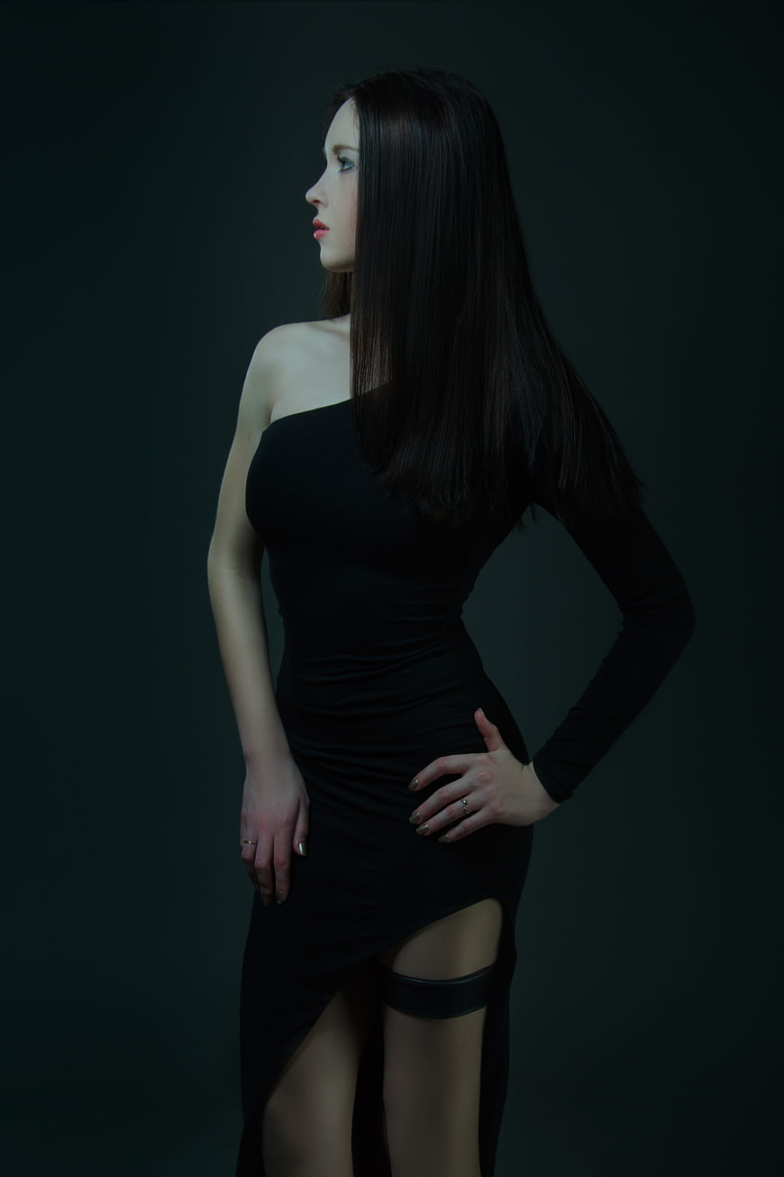 Elegant young woman in black one-shoulder dress against dark background
