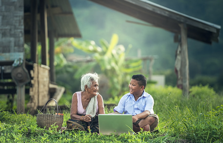 Senior woman and boy using laptop in rural village