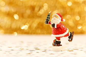 Santa Claus Figurine Skating with Christmas Tree on Gold Bokeh Background