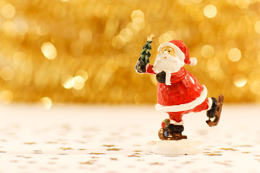 Santa Claus Figurine Skating with Christmas Tree on Gold Bokeh Background