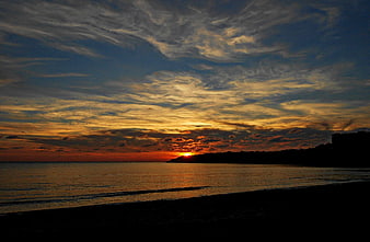 Dramatic sunset over calm sea with textured clouds and silhouette