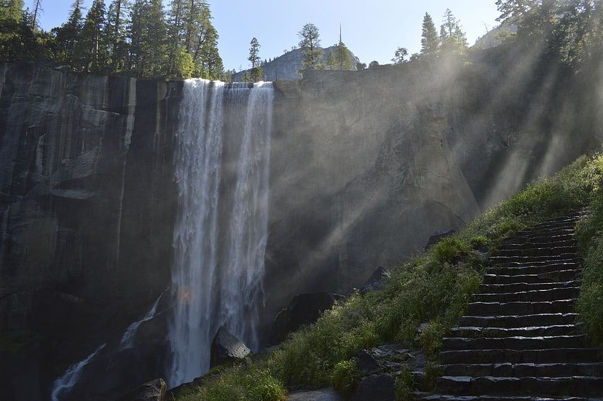 Majestic waterfall with sunbeams and stone stairs in forest