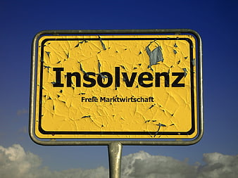 Weathered yellow sign reading Insolvency against blue sky