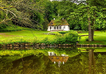 Charming white cottage with moss roof reflected in pond