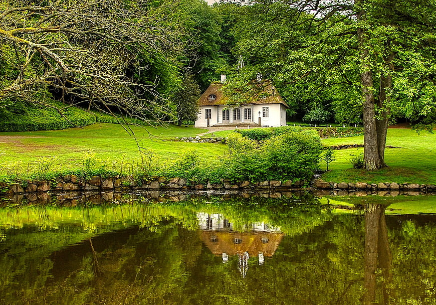 Charming white cottage with moss roof reflected in pond