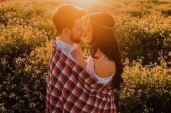 Romantic couple wrapped in plaid blanket in golden field