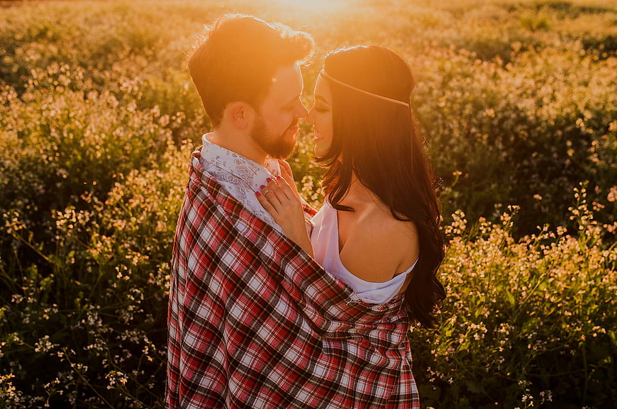 Romantic couple wrapped in plaid blanket in golden field