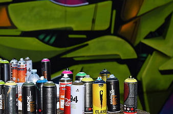 Collection of spray paint cans in front of graffiti wall