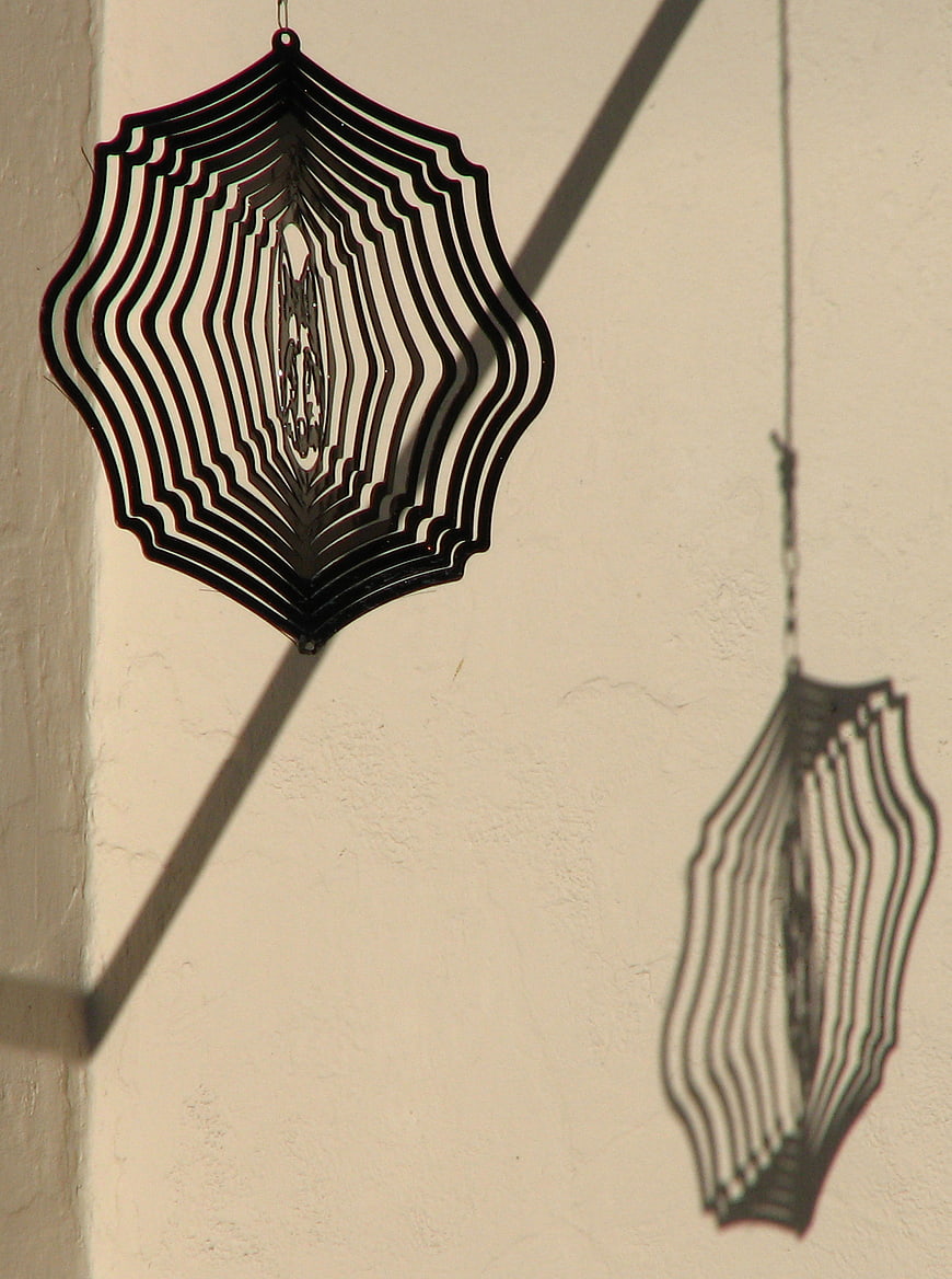 Black metal spider web mobile casting shadow on wall