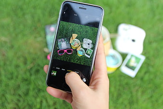 Hand holding smartphone taking photo of picnic items on grass