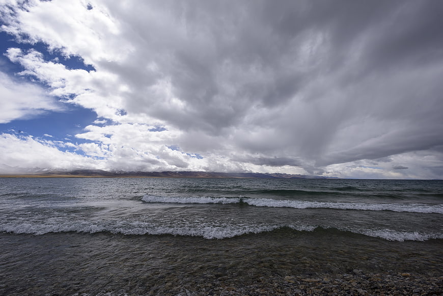 Dramatic Clouds Over a Rocky Lake Shore with Distant Mountains