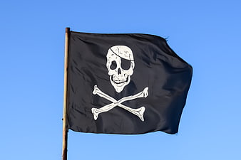 Black pirate flag with skull and crossbones waving against blue sky