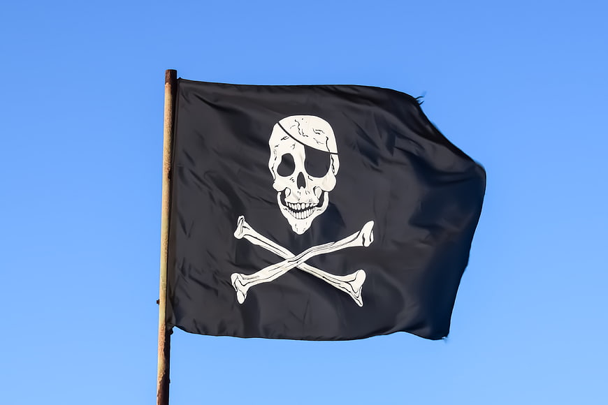 Black pirate flag with skull and crossbones waving against blue sky