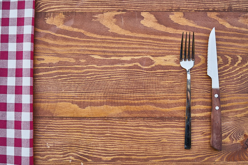 Fork and knife on wooden table with red checkered napkin