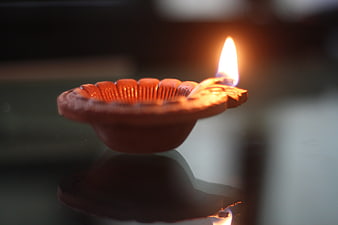 Traditional clay diya lamp with flame on reflective surface