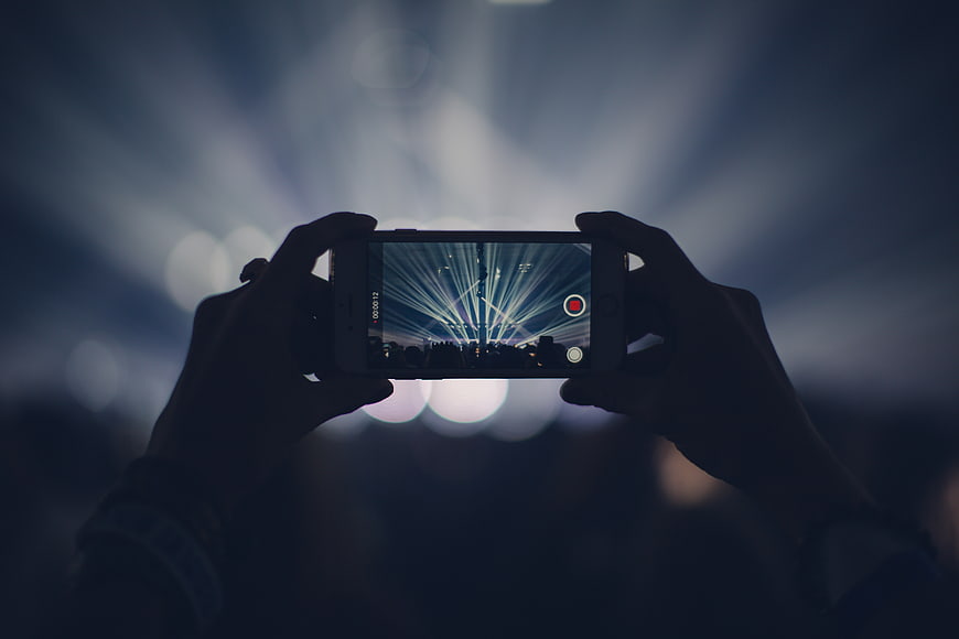 Hands holding smartphone recording concert stage lights