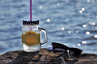 Mason jar drink with lemon and sunglasses on a rock by the water