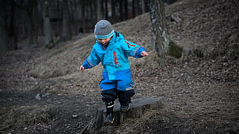 Toddler in Blue Rain Suit Balancing on Tree Stump in Forest