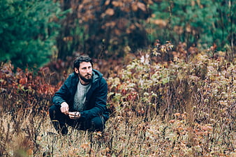Bearded man crouching in autumn forest foliage