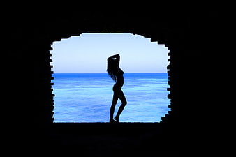 Silhouette of woman in bikini framed by archway against blue ocean