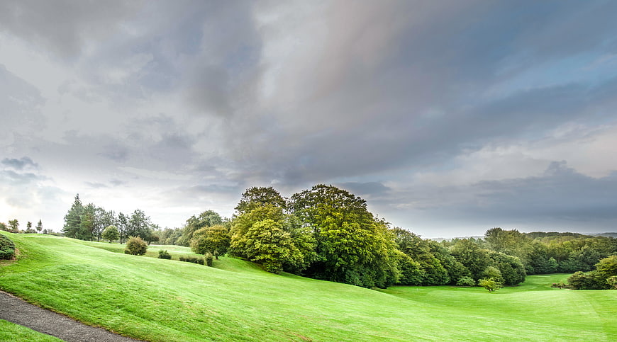 Lush green golf course landscape with dramatic cloudy sky