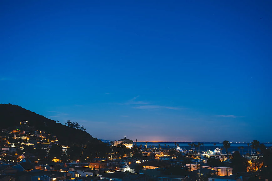 Nighttime coastal cityscape with hillside homes and ocean view