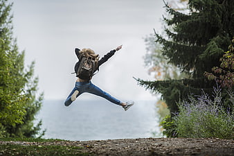 Woman jumping with backpack in nature near ocean
