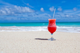 Red Tropical Cocktail on Sandy Beach with Ocean Background