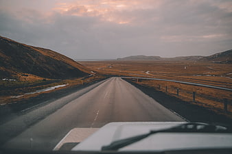 Car driving on scenic road through vast landscape at sunset