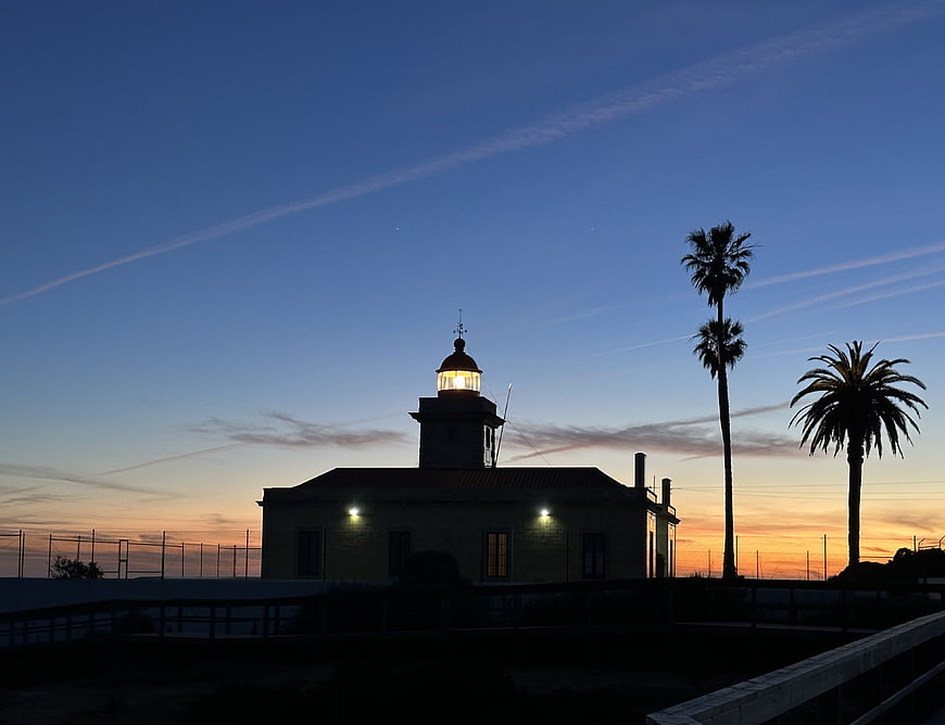Lighthouse Silhouette at Dusk with Palm Trees and Sunset Sky