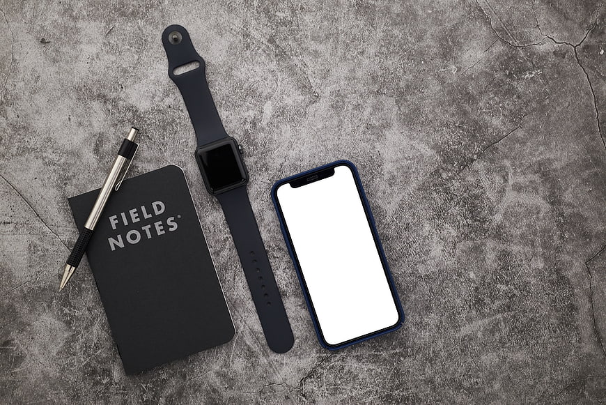 Flat lay of smartphone, smartwatch, and notebook on concrete