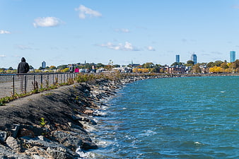 People walking on rocky waterfront path with city skyline