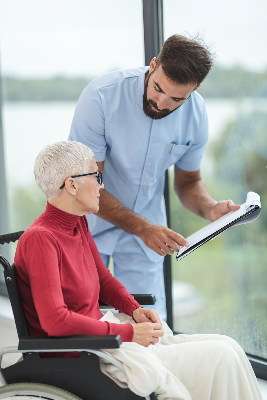 Male nurse discussing medical records with elderly woman in wheelchair