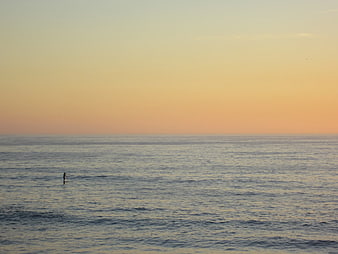 Lone paddleboarder on calm ocean during golden hour sunset