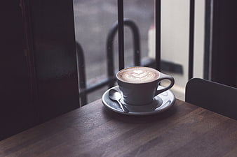 Latte with heart art on wooden table by window
