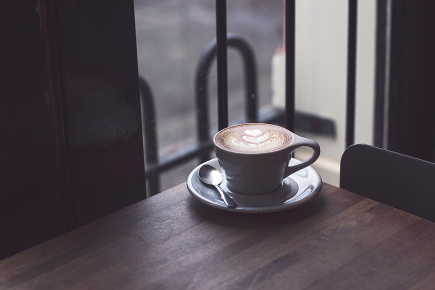 Latte with heart art on wooden table by window