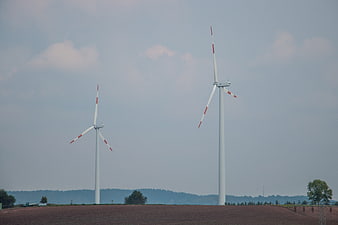 Two wind turbines on a hill against a cloudy sky
