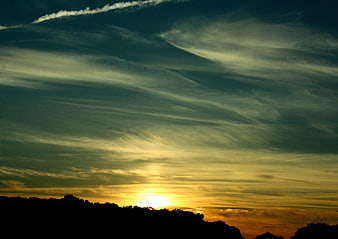 Dramatic sunset sky with wispy clouds over silhouetted treeline