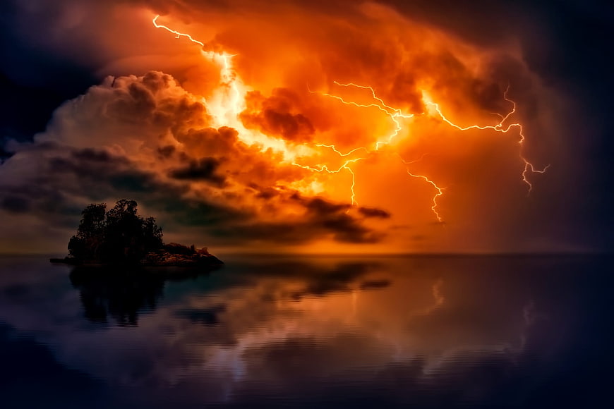 Dramatic orange lightning storm over ocean with island silhouette