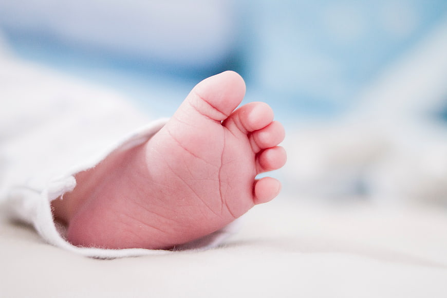 Close-up of a newborn baby's tiny foot wrapped in white blanket
