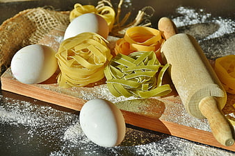 Fresh handmade pasta nests, eggs, and rolling pin on wooden board