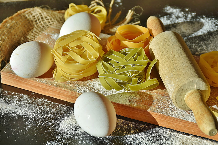 Fresh handmade pasta nests, eggs, and rolling pin on wooden board